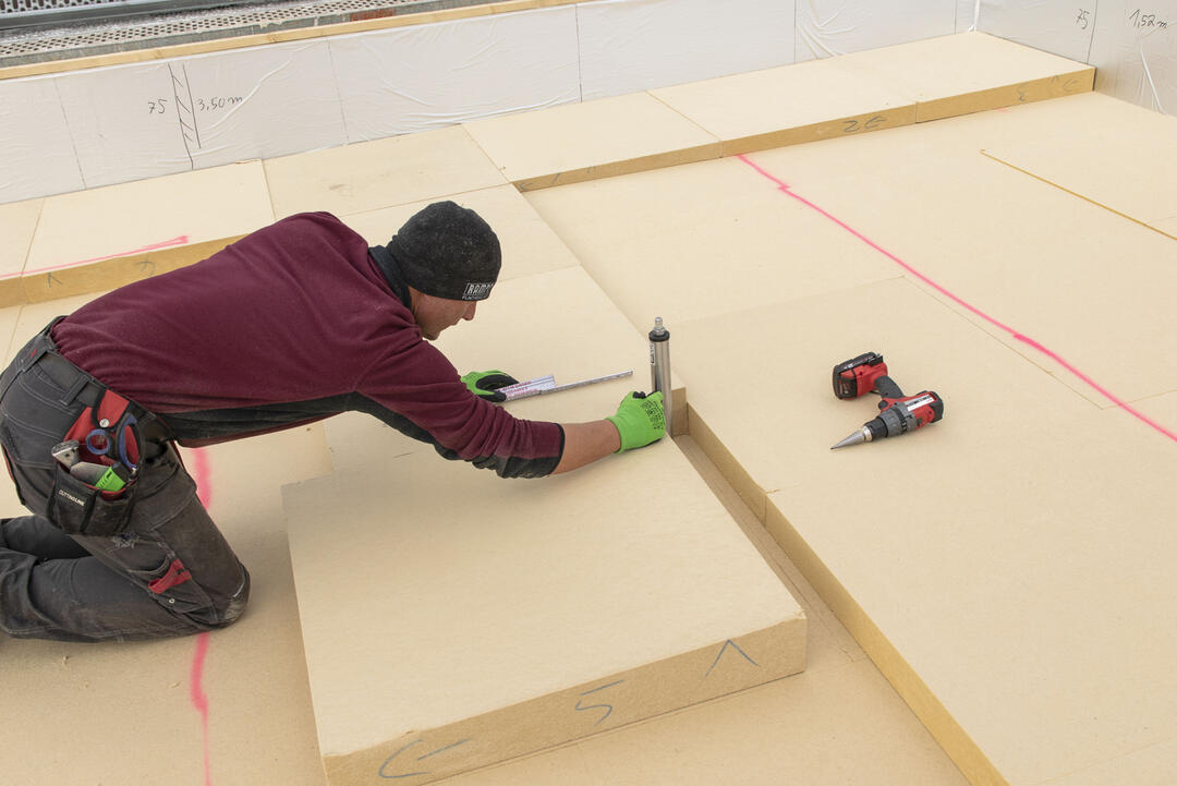 Ein Handwerker bringt die Platten auf ein Flachdach und markiert mit einem Stift einen Punkt auf der Fläche.