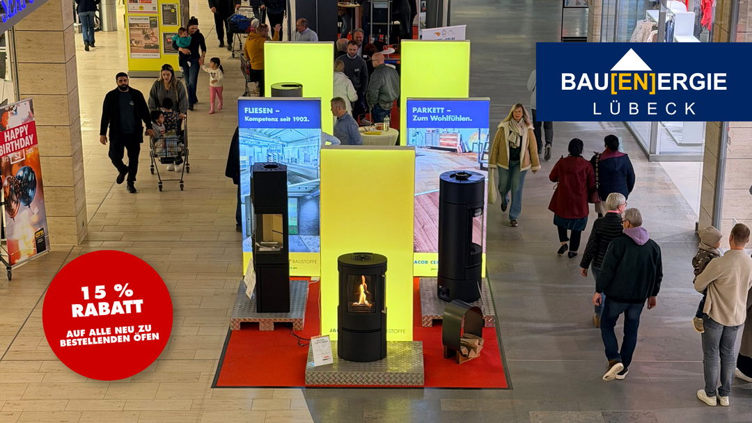 Bildausschnitt eines Fotos von den Bauenergietagen 2025 im CITTI-PARK in Lübeck mit herumflanierenden Menschen und ausgestellten Kaminöfen, von oben fotografiert. Oben rechts eingeblendet ist das Logo der Messe, unten links ein roter Störer, der auf das 15 Prozent-Rabatt-Angebot für Messerbesucher hinweist.