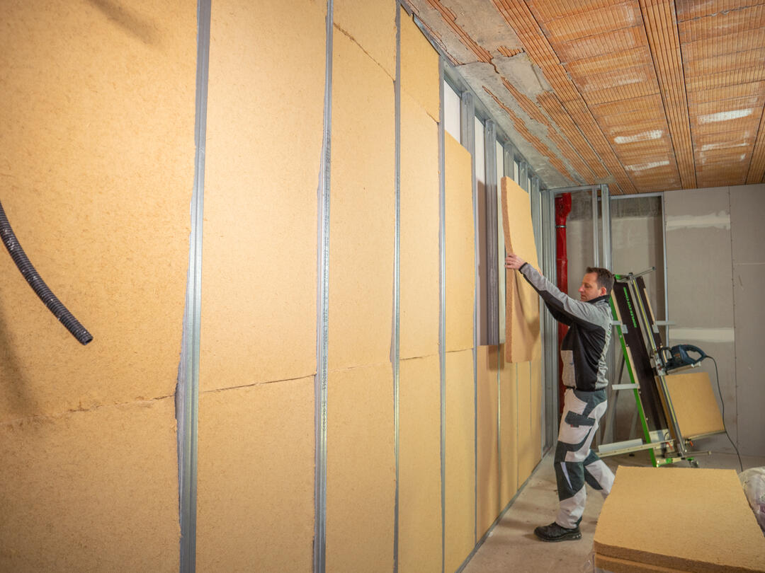 Ein Mann verlegt in einem Innenraum STEICOflex-Platten. Die Wand ist bereits fast vollständig mit STEICOflex gedämmt.