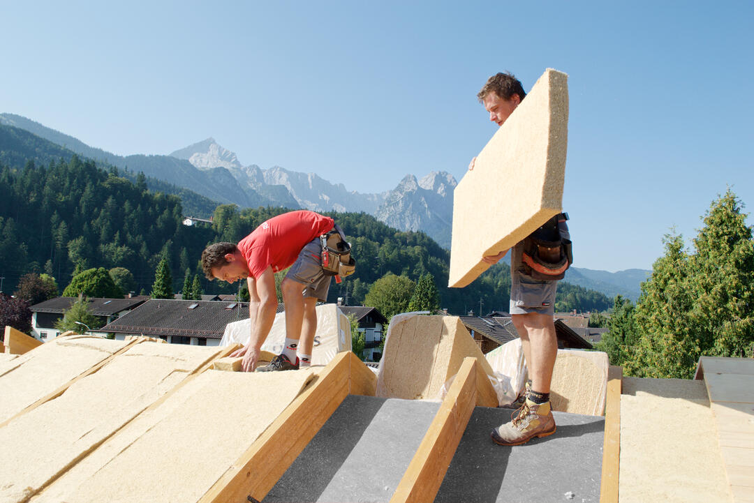 Zwei Männer arbeiten auf einem Dach unter blauem Himmel. Sie bringen STEICOflex-Dämmplatten außen aufs Dach auf.
