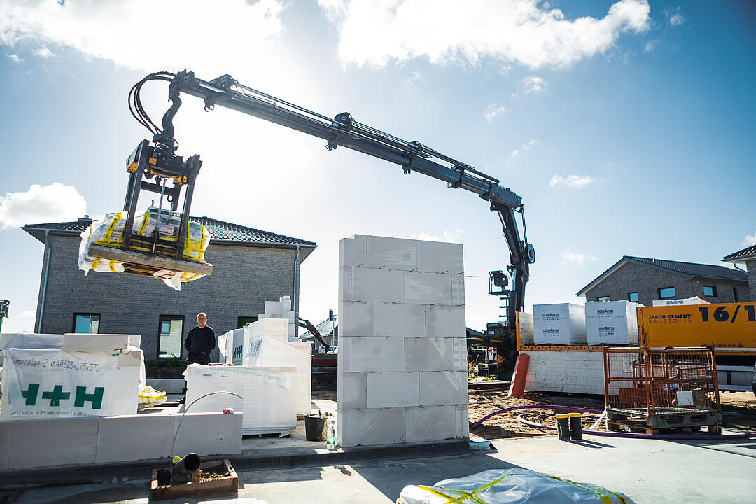 Ein LKW von JACOB CEMENT BAUSTOFFE entlädt mithilfe des integrierten Ladekrans eine Palette Kalksandstein passgenau in den Rohbau auf einer Baustelle