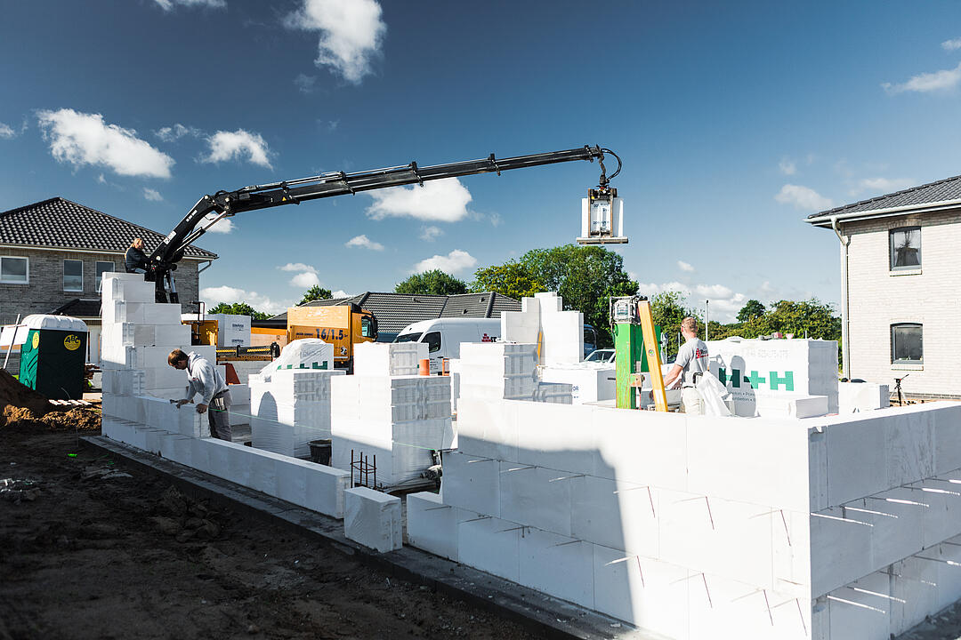Ein LKW von JACOB CEMENT BAUSTOFFE entlädt mithilfe des integrierten Ladekrans eine Palette Kalksandstein auf einer Baustelle