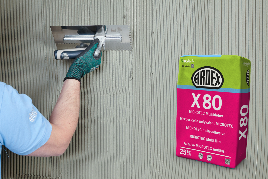 Eine Fotomontage: Den Hintergrund bildet eine Wand, auf die von einer Hand mit einem Werkzeug Fliesenkleber der Marke Ardex aufgetragen wird. Die Masse ist hellgrau. Im Vordergrund rechts ist ein Sack des Produkts eingeblendet, grün und pink mit der Aufschrift X 80.