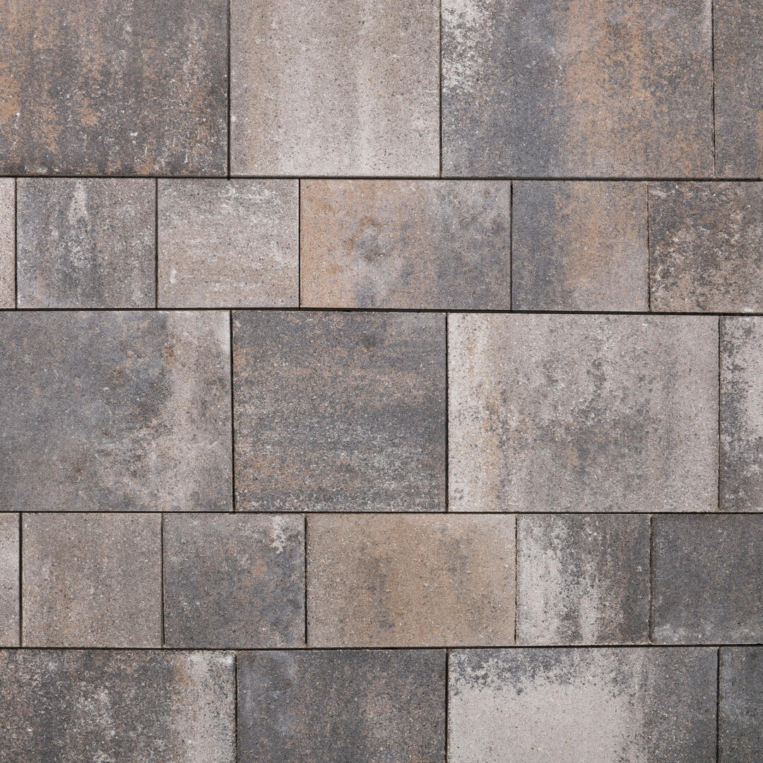 Blick von oben auf eine gepflasterte Fläche. Große Pflasterplatten wechseln sich mit kleineren Platten ab, was ein interessantes Verlegebild ergibt. Das braun-grau-rötliche Pflaster wirkt rustikal und beständig.