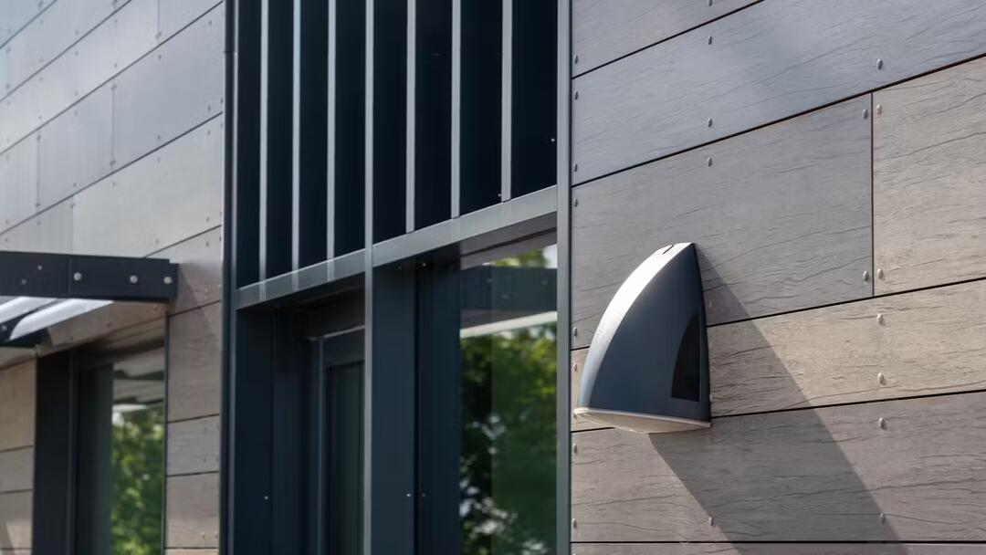 Ausschnitt einer Fassade aus Rockpanel-Fassadenplatten in dunkler Holzoptik mit einem Eingangsbereich in dunklen Farben und einer an der Wand angebrachten Lampe.