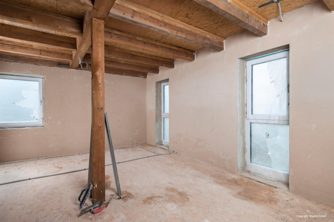 Ein mit dem Produkt sanierter Raum mit nun beigen Wänden und einer rustikalen Holzbalkendecke.