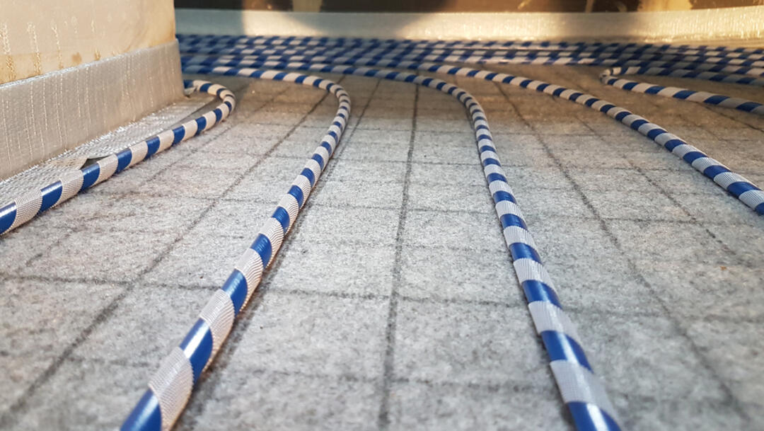 Nahaufnahme eines Permatop-Heizsystems von Blanke im Prozess des Einbaus. Blau-weiß geringelte Rohre laufen über den gefliesten Boden und um eine Kurve.