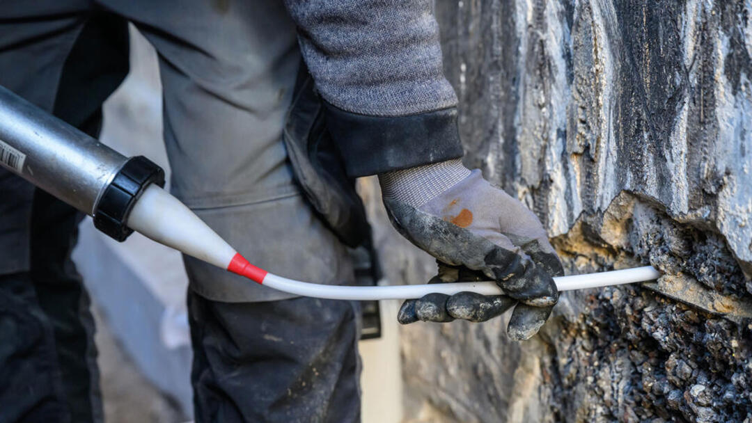Praxisfoto: Eine Person verkieselt die sanierungsbedürftige Wand mit einer speziellen Spritze. Von der Person sind nur Beine und Hand zu sehen.