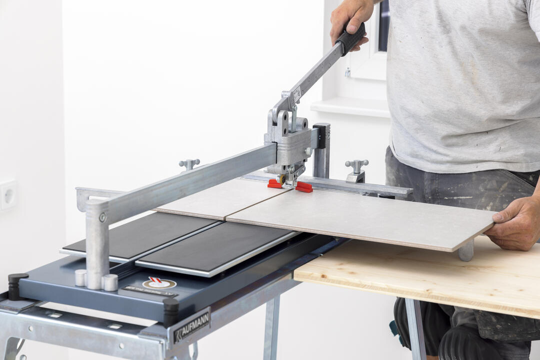 Nahaufnahme einer Topline Pro-Fliesenschneidemaschine bei der Anwendung. Eine Person hält mit einer Hand den Hebel und mit der anderen die zu durchtrennende Fliese.