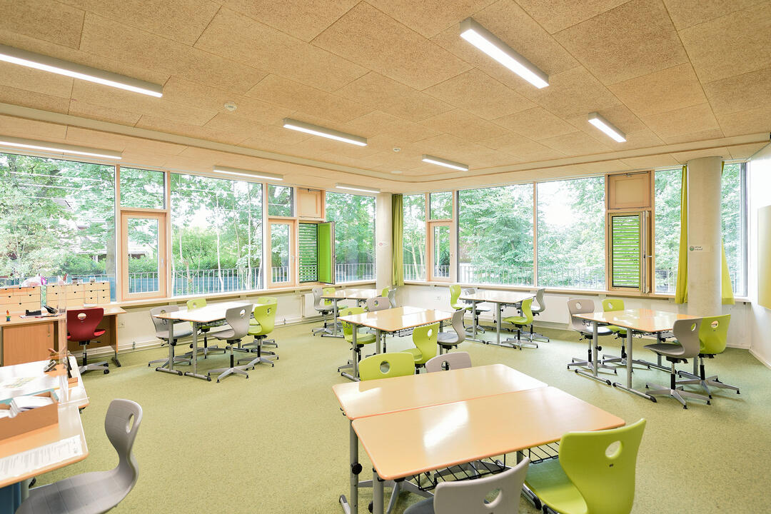 Ein heller, freundlicher Klassenraum in einer Grundschule, mit Gruppentischen und bunten Stühlen.