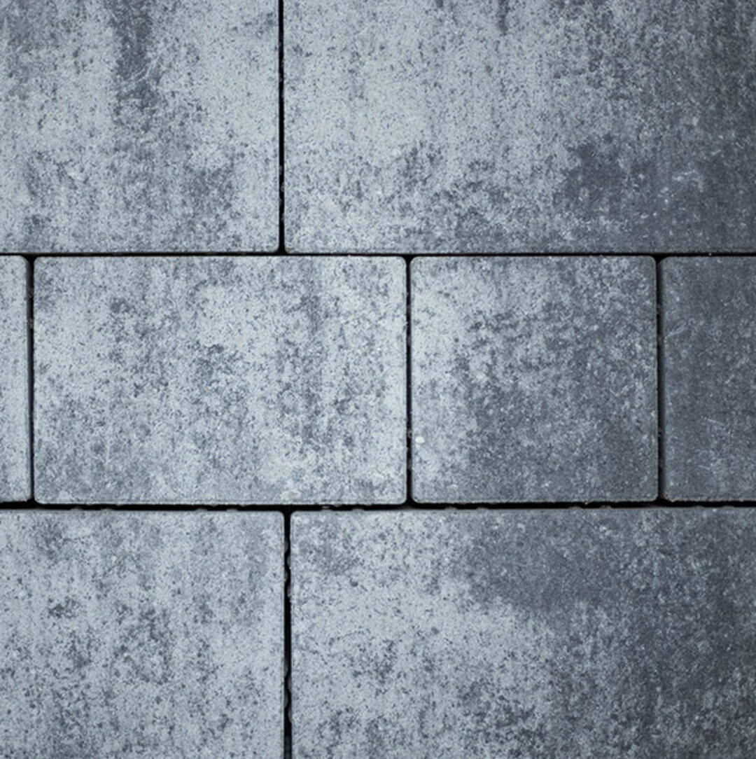 Blick von oben auf eine gepflasterte Fläche. Große Pflasterplatten wechseln sich mit kleineren Platten ab, was ein interessantes Verlegebild ergibt. Das graue Pflaster wirkt rustikal und beständig.