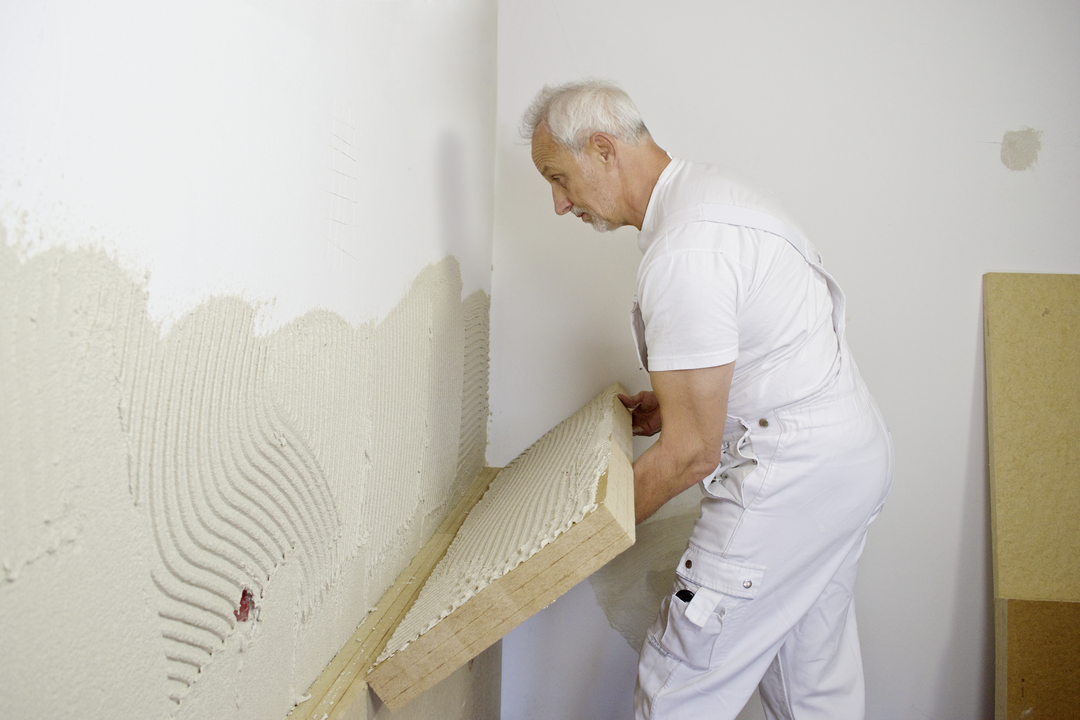 Ein Handwerker in weißer Arbeitskleidung bringt eine Platte der STEICO-Innendämmung an einer Wand an.