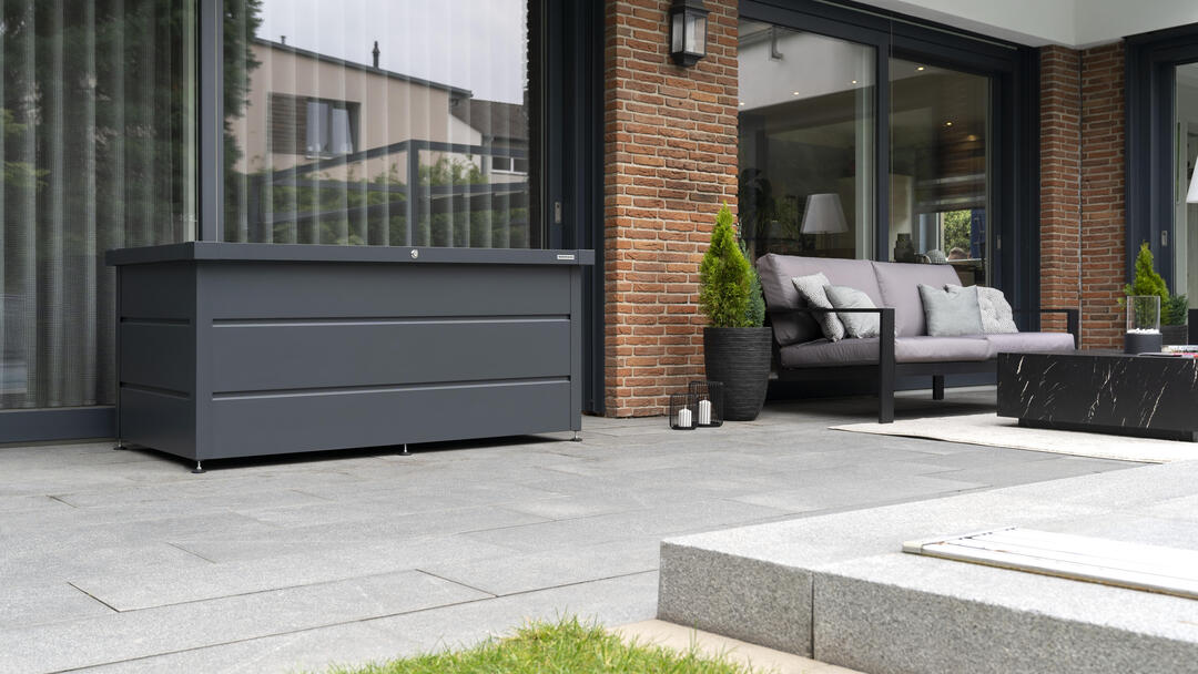 Eine Terrasse, auf der eine schwarze Gerätebox von Hörmann vor einer großen Fensterfront steht.