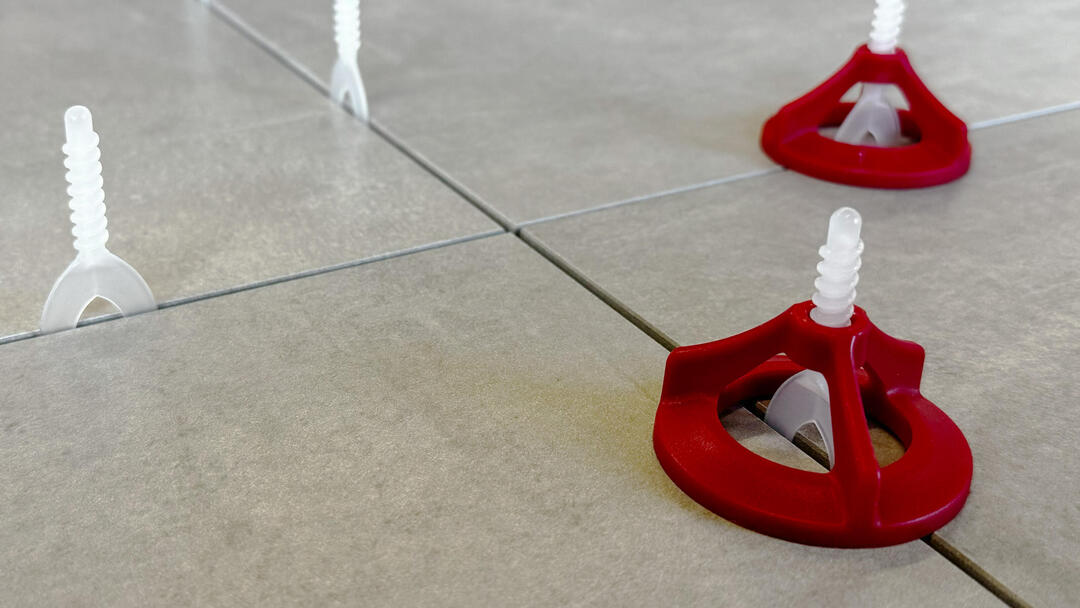 Das Ceratec-Nivelliersystem in der Nahaufnahme: Zwischen akkurat verlegten hellgrauen Fliesen stecken weiße und rote Trennelemente.