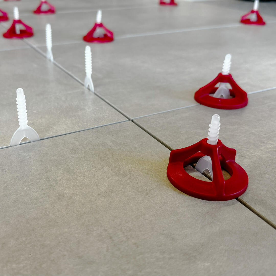 Das Ceratec-Nivelliersystem in der Nahaufnahme: Zwischen akkurat verlegten hellgrauen Fliesen stecken weiße und rote Trennelemente.