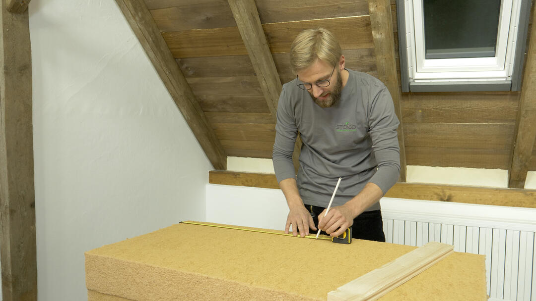 Ein Mann misst an einem STEICOflex-Block ab, wieviel Material er braucht.